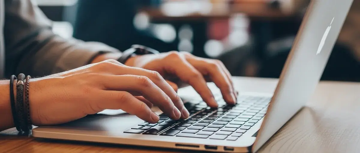 Close-up of hands typing on a laptop in a bustling hostel, symbolizing remote work